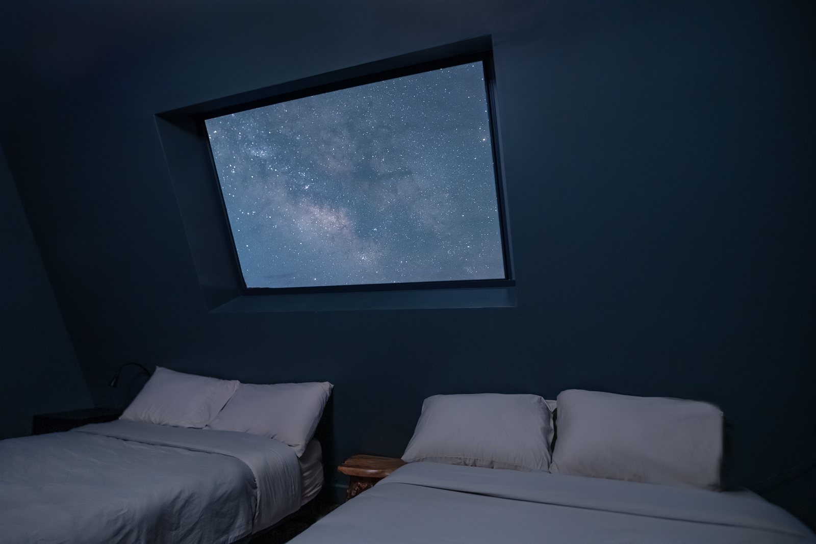 Stars and the Milky Way seen through an A-frame bedroom window above two beds